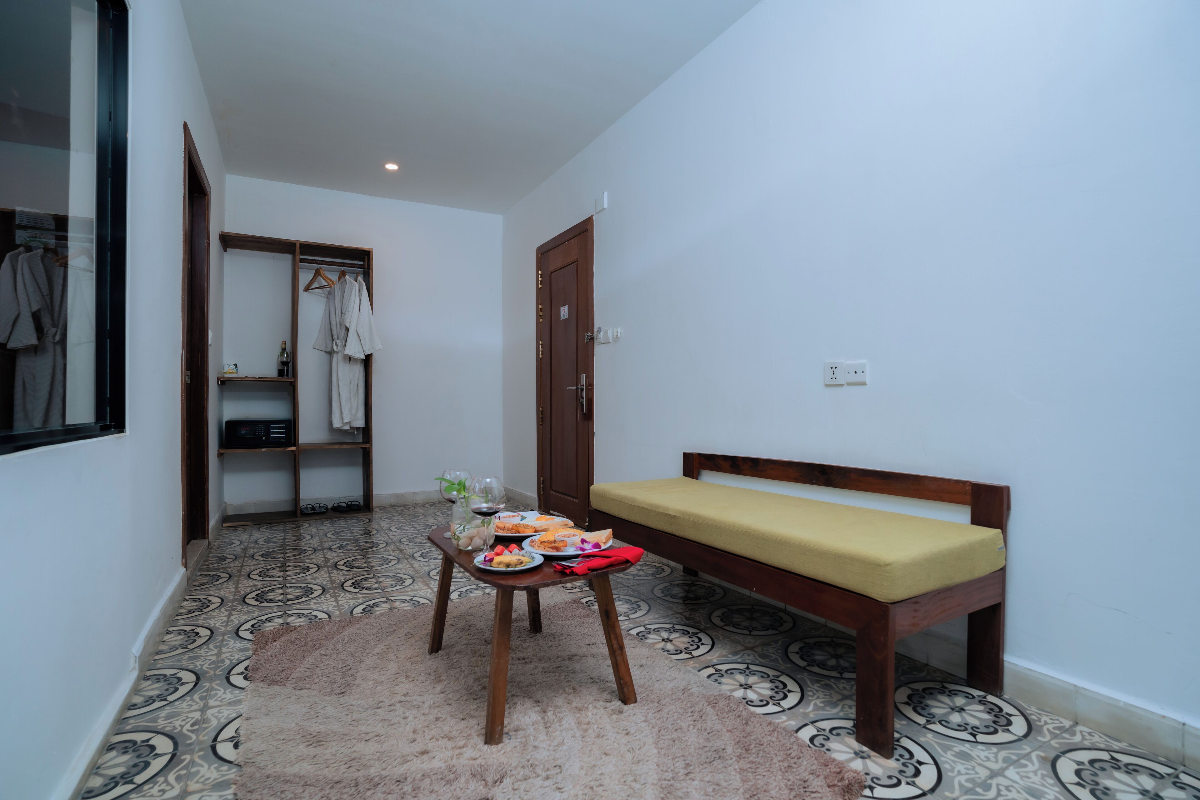 Una habitación pequeña con una banca, una mesa con comida y bebidas, un perchero y una puerta.