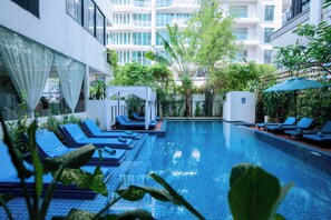 Una piscina con sillas reclinables azules y un edificio blanco al fondo.
