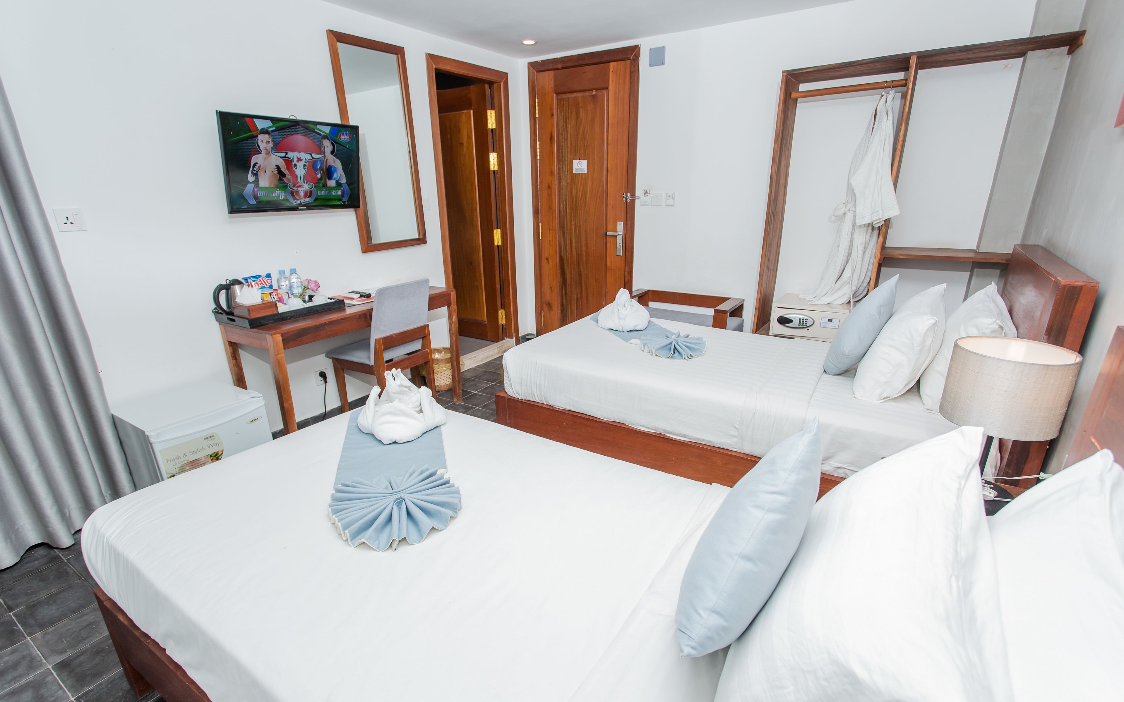 A hotel room with two beds, a desk, a chair, a TV, and a bathroom.
