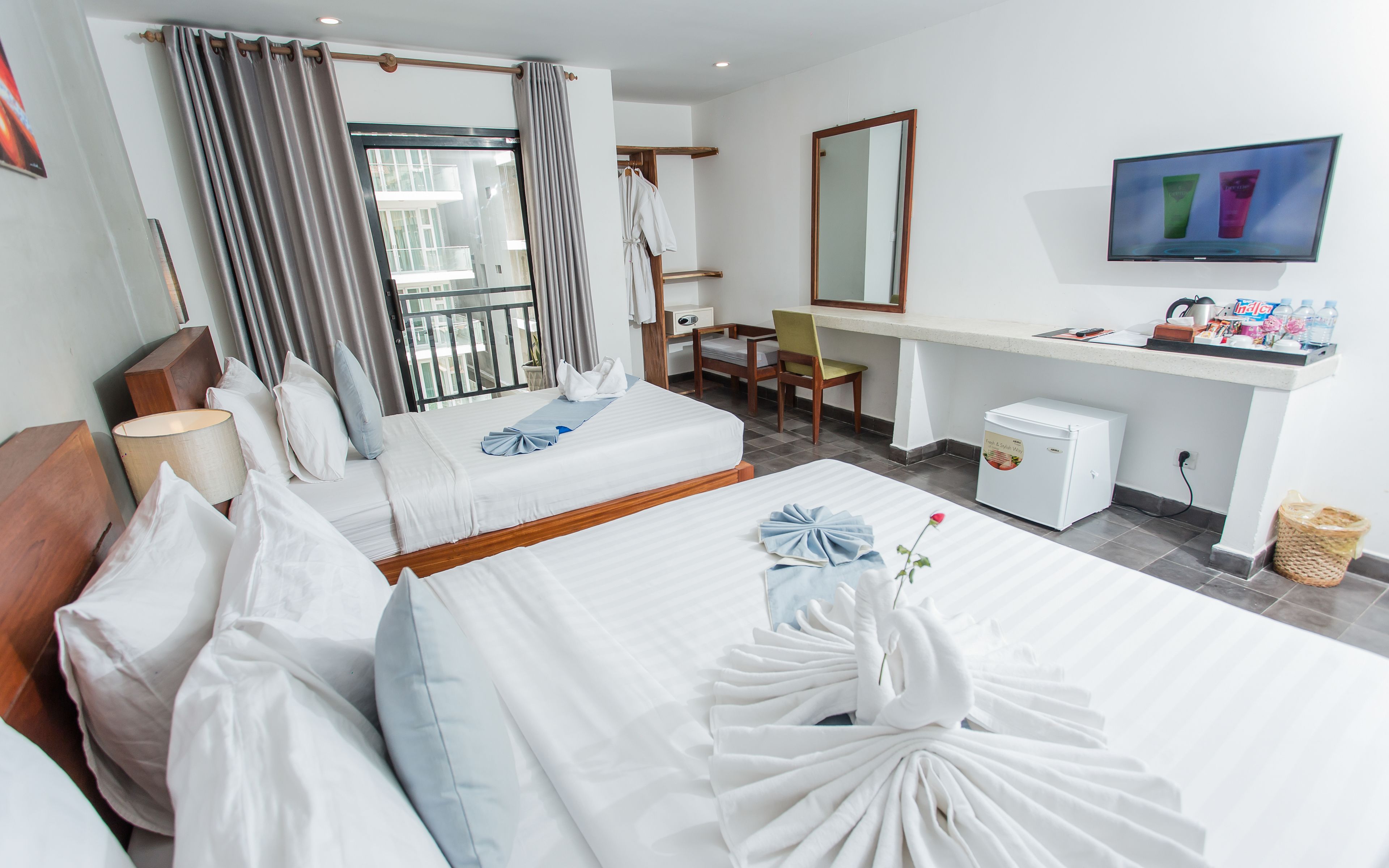 A hotel room with two beds, a desk, a chair, a television, and a small refrigerator.
