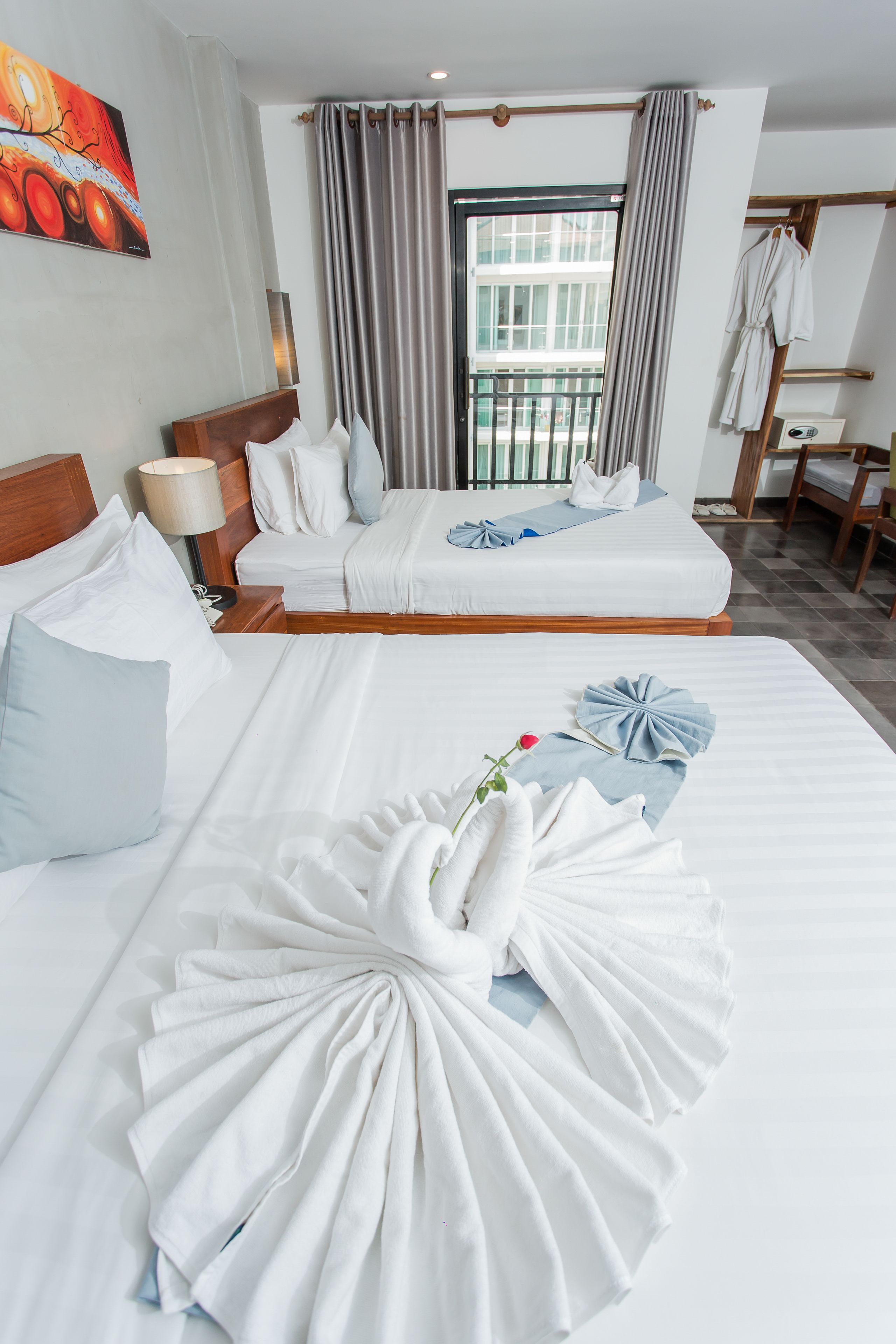 A hotel room with two beds, a large window, and a painting on the wall.