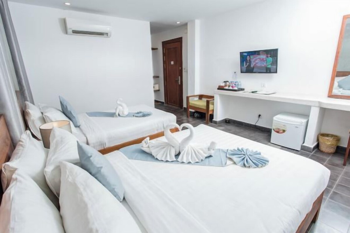 A hotel room with two beds, a desk, a TV, and a small kitchenette.