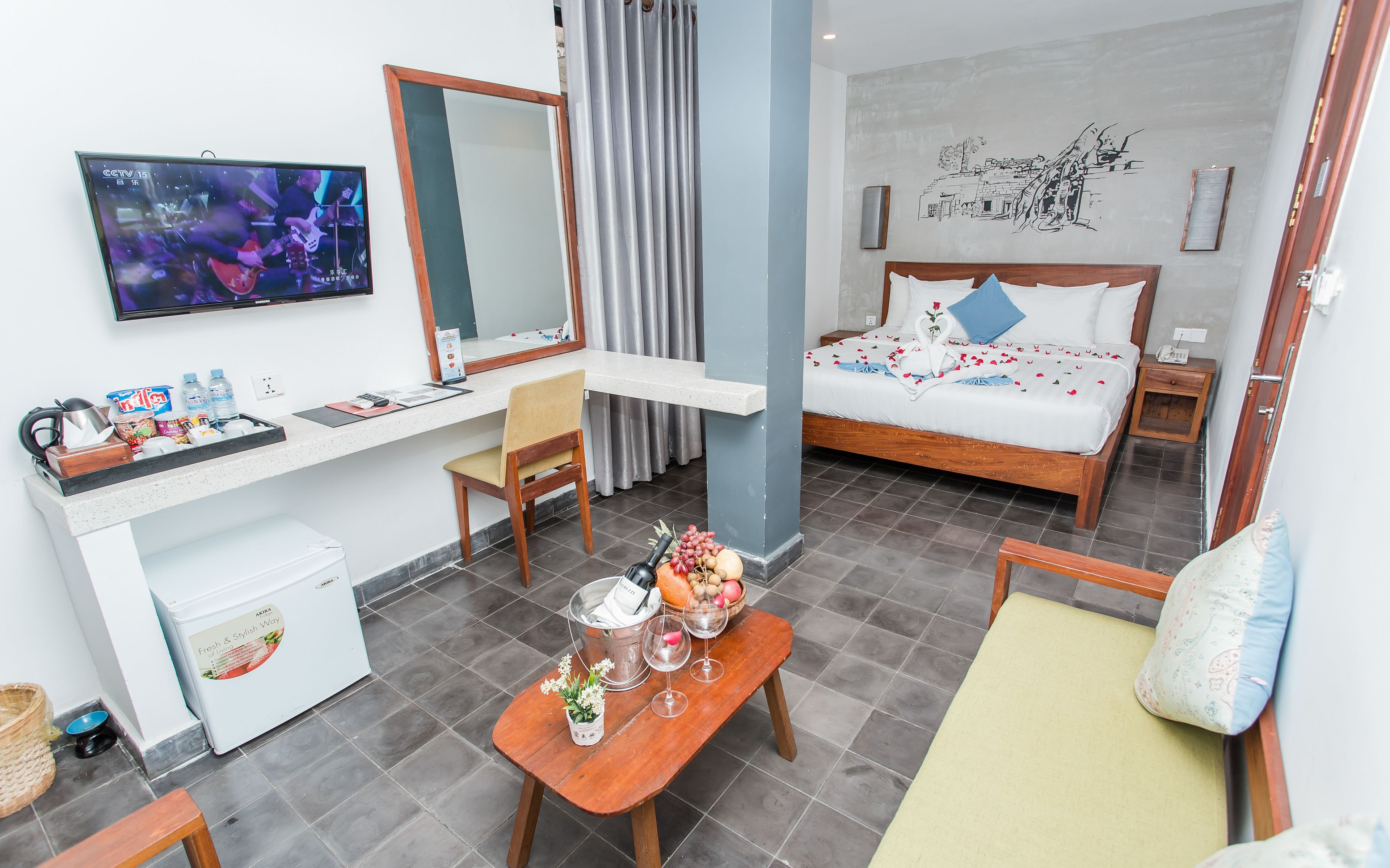 Ein Hotelzimmer mit Bett, Schreibtisch, Stuhl, einem kleinen Tisch mit Speisen und Getränken, einem Fernseher und einer Wand mit Wandgemälde.