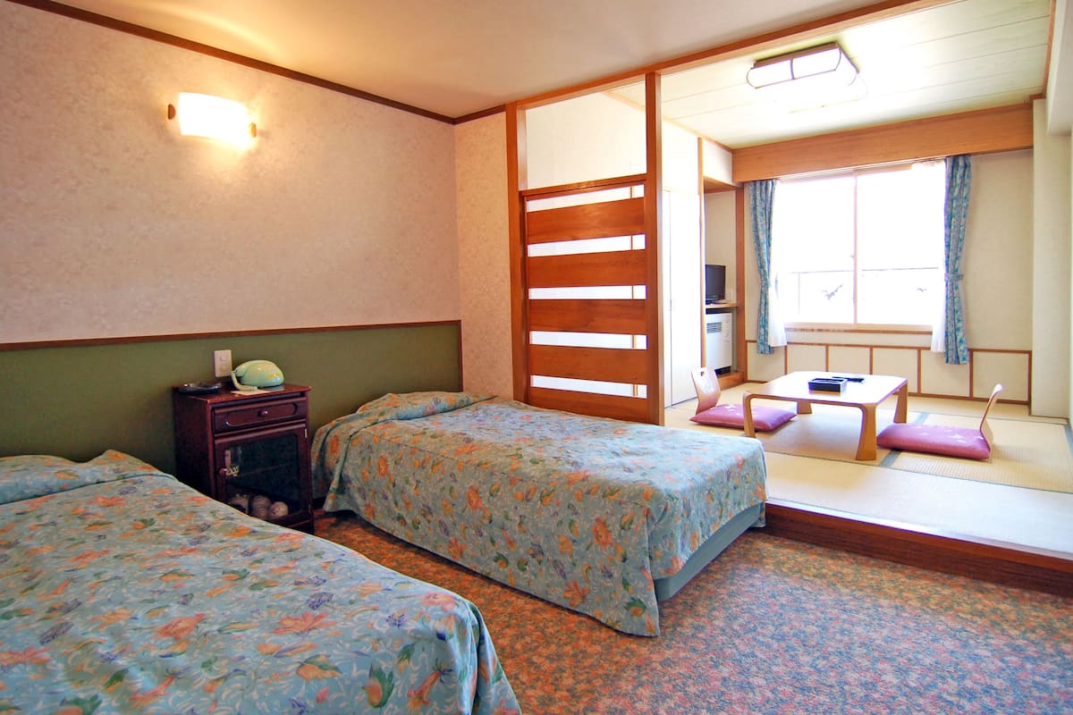 A hotel room with two beds, a desk, and a window with curtains.