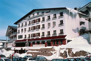 Hotel com vários andares e varandas, pista de esqui em frente e chão coberto de neve.