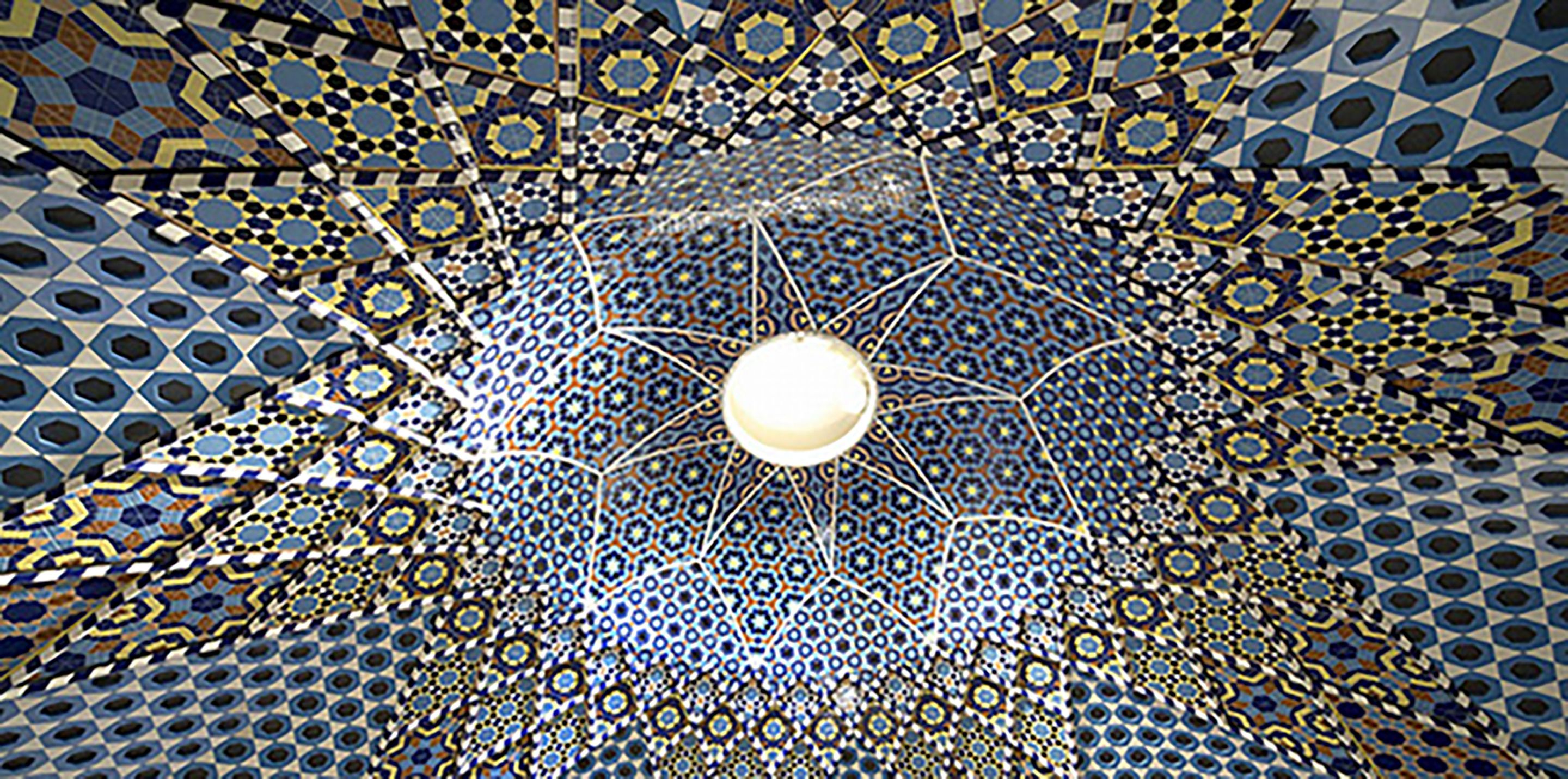 A detailed ceiling with a central spherical light fixture surrounded by intricate geometric patterns.