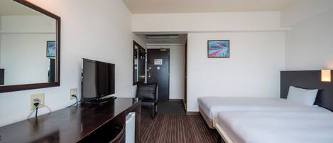 A hotel room with a bed, a desk with a television, a chair, and a door leading to a hallway.