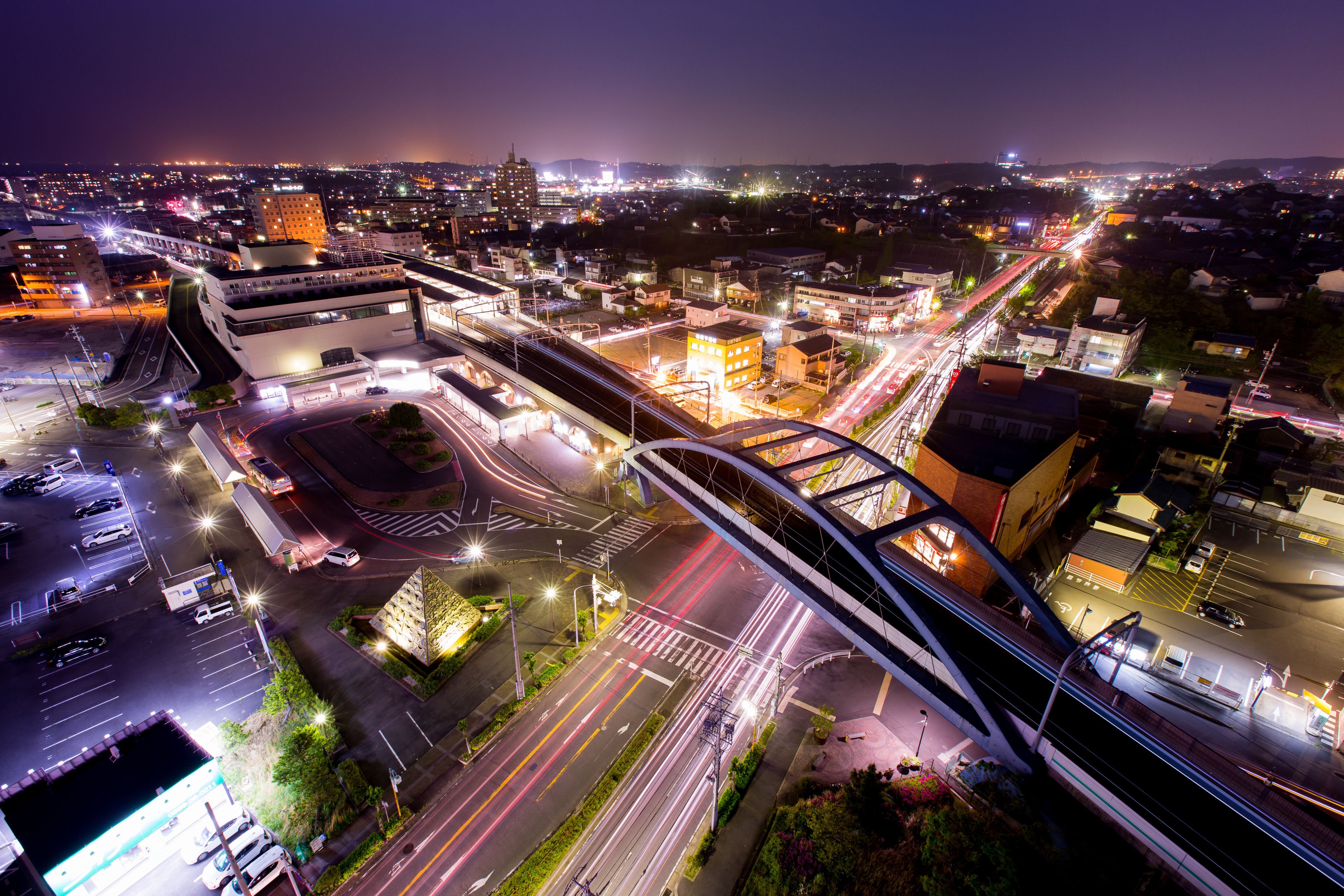 An aerial view of a cityscape at night with illuminated buildings, roads, and a bridge.