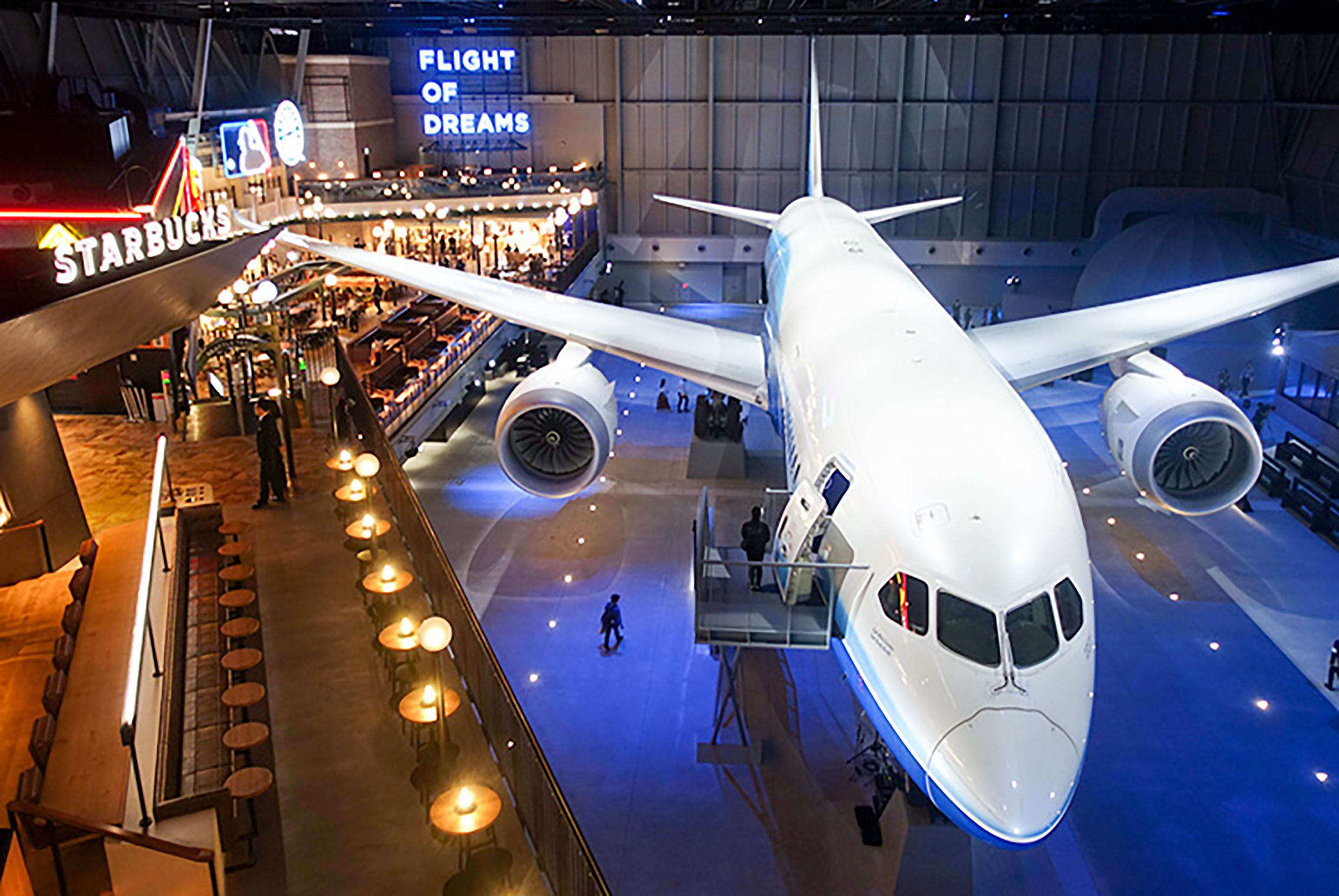 A large airplane displayed indoors with a Starbucks sign and a 'Flight of Dreams' sign in the background.