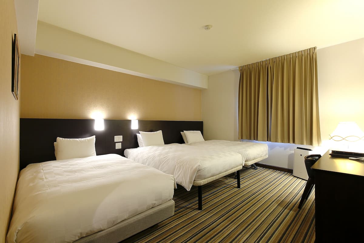 A hotel room with two beds, a desk, and a large window with curtains.
