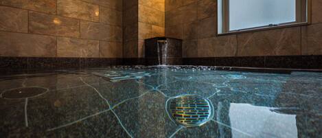 A modern indoor swimming pool with a geometric tile design, a water feature, and a large window.