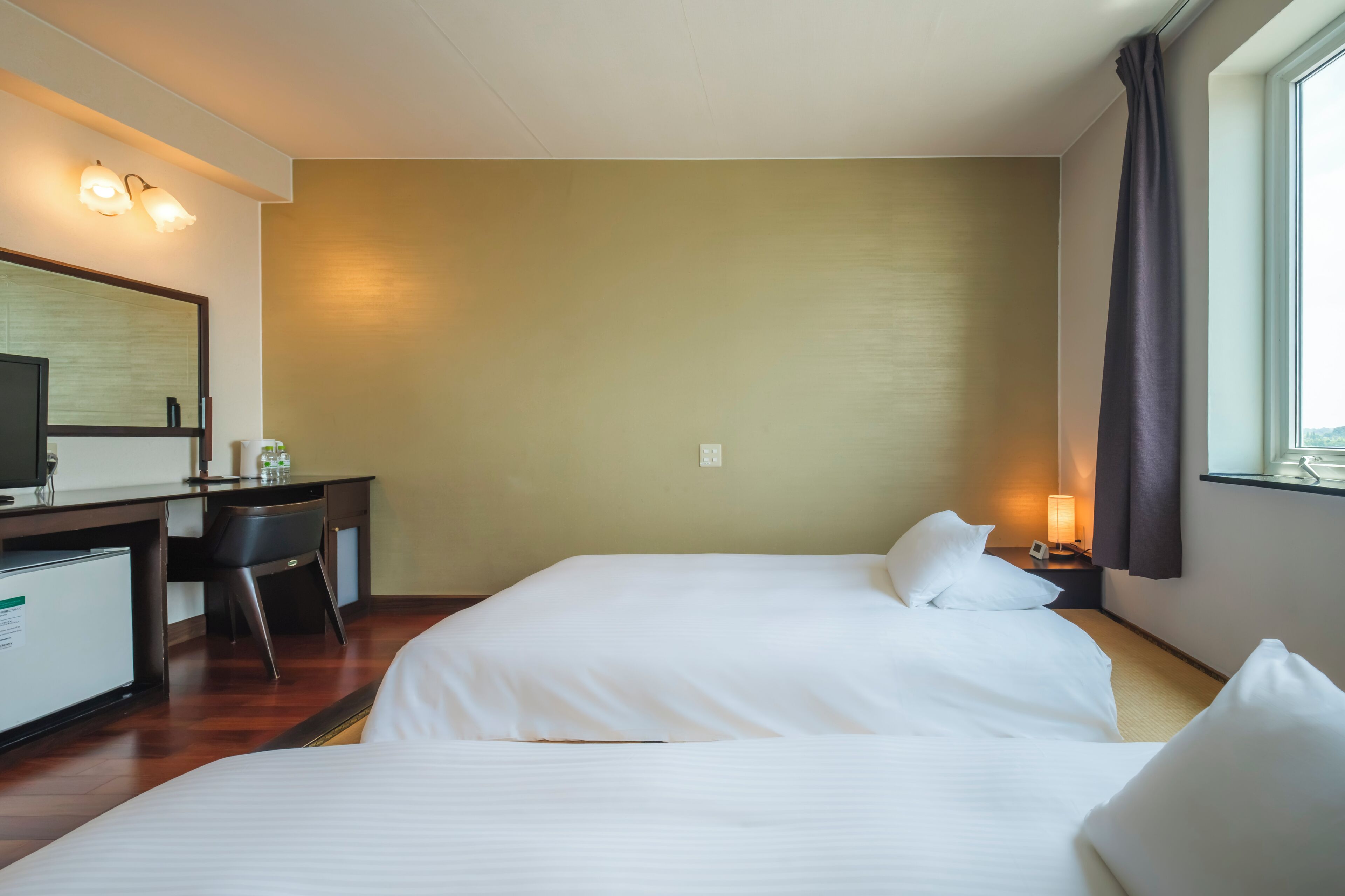 A hotel room with a bed, a desk, a chair, a television, and a window with curtains.