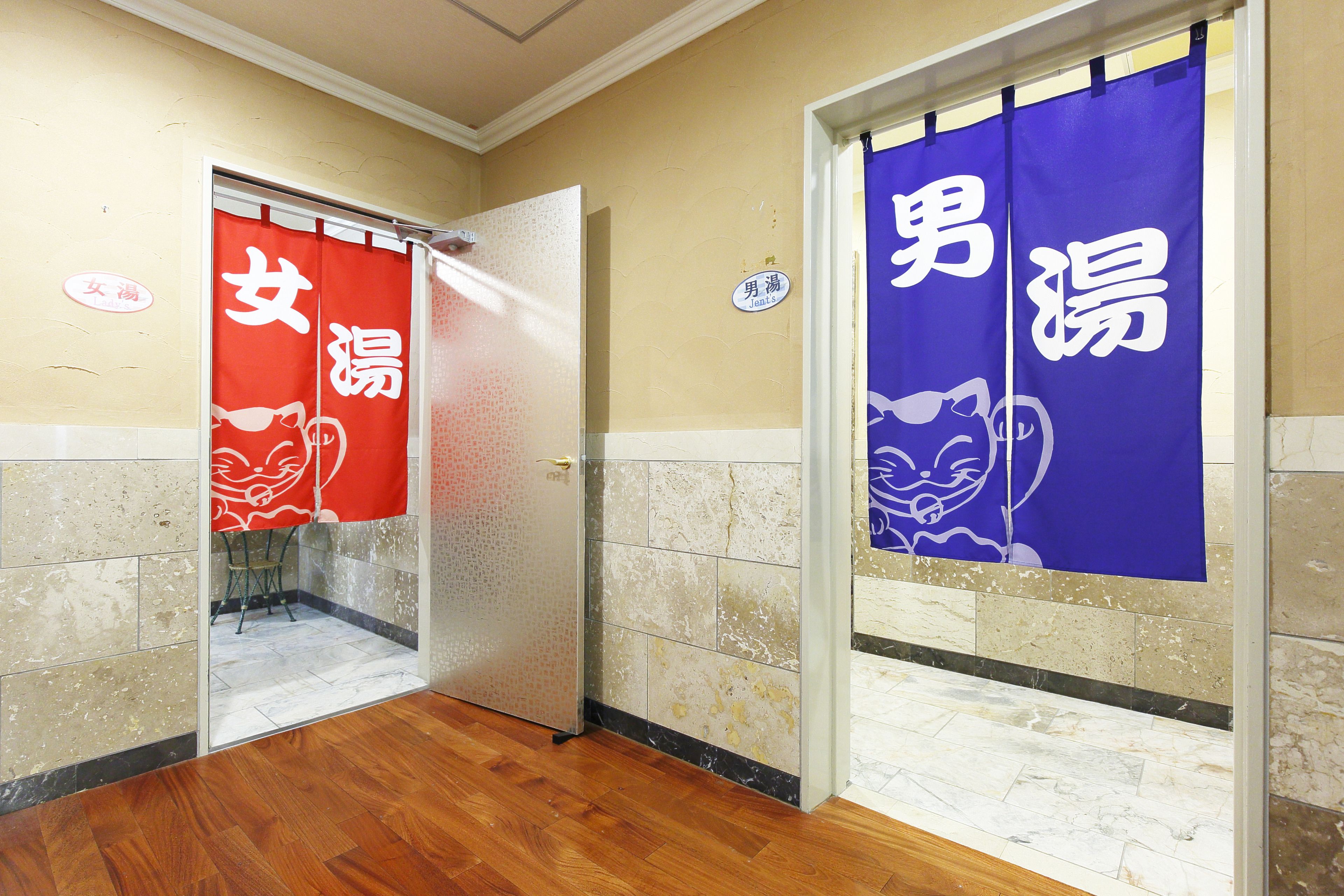 Un pasillo con dos puertas, una con cortina roja y la otra con cortina azul, cada una decorada con una ilustración de un gato y caracteres chinos.