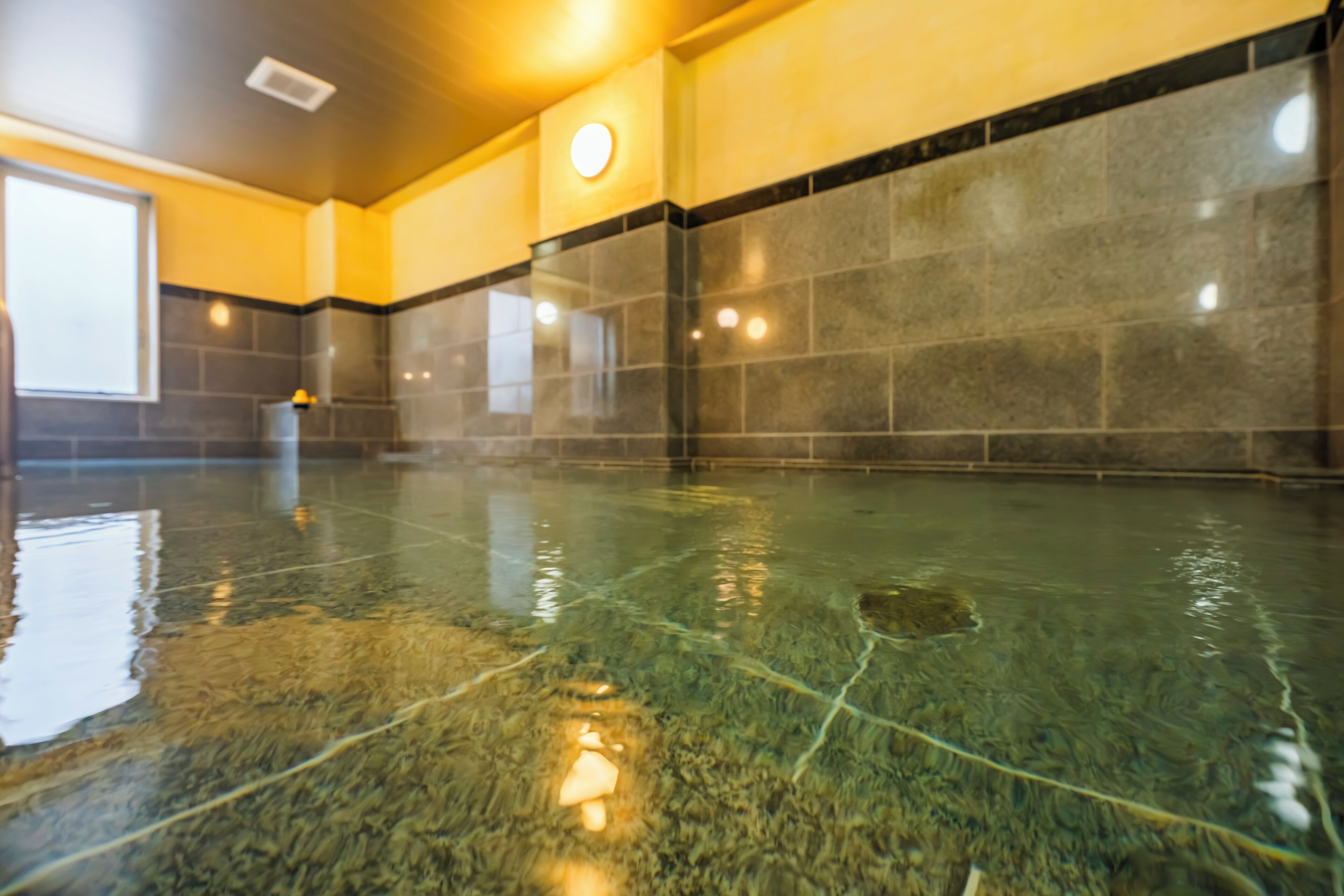 Piscina con agua cristalina, rodeada de paredes con azulejos e iluminación empotrada en el techo.