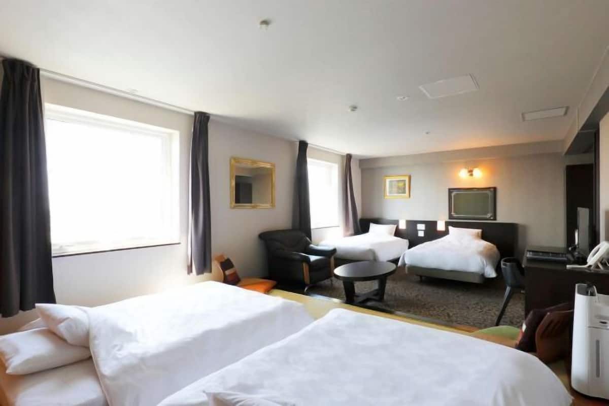 A hotel room with two beds, a desk, a chair, a small table, and a television.