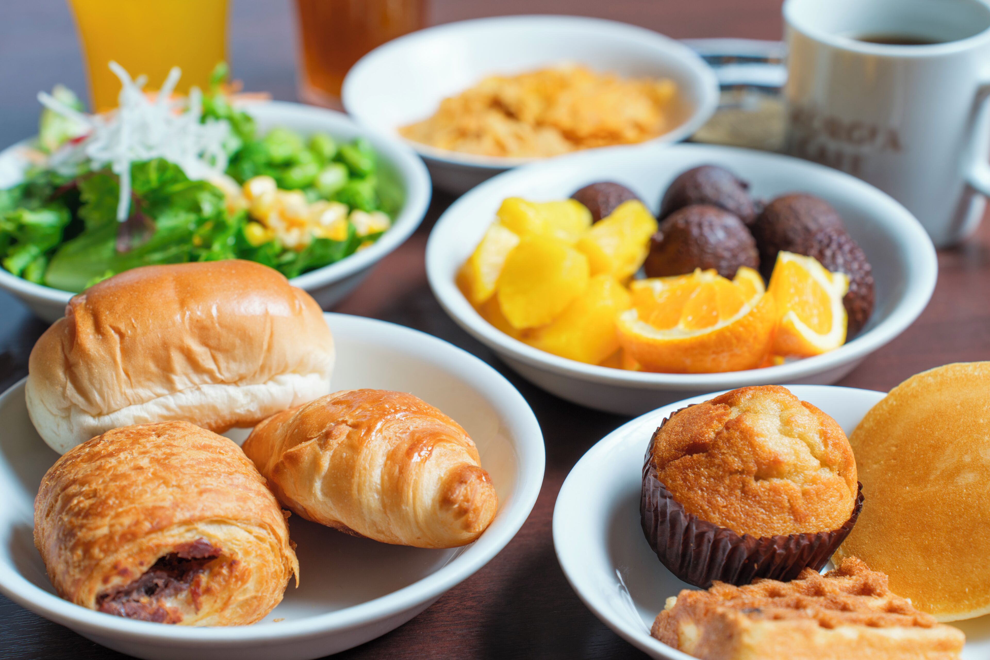 Variedad de opciones para el desayuno, incluyendo pasteles, frutas y una ensalada sobre una mesa.