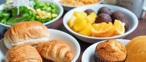 Variedad de opciones para el desayuno, incluyendo pasteles, frutas y una ensalada sobre una mesa.