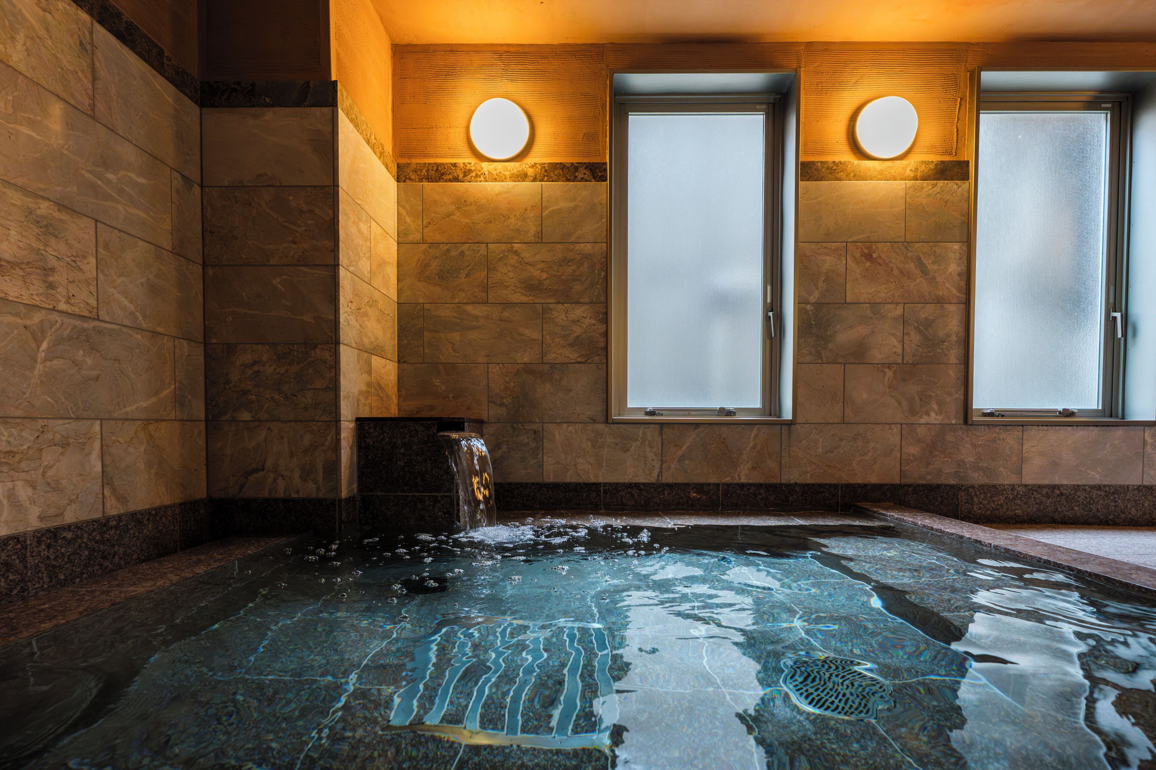 Un cuarto de spa con un jacuzzi, dos puertas de vidrio satinado y un aplique de pared.