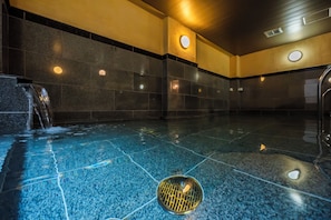 A swimming pool with a water feature, tiled walls, and recessed lighting.
