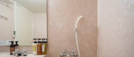Un baño con lavamanos, espejo, artículos de aseo y ducha.