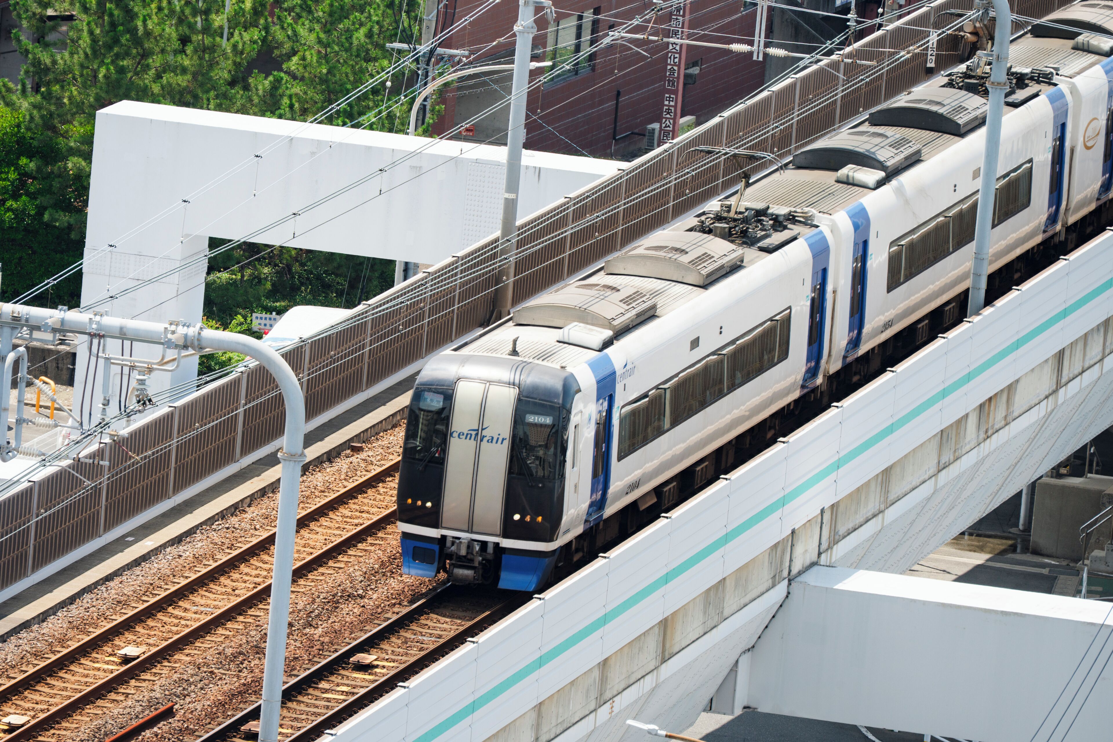 Ein Zug auf einer erhöhten Trasse mit modernem Design, umgeben von Infrastruktur und Grünflächen.