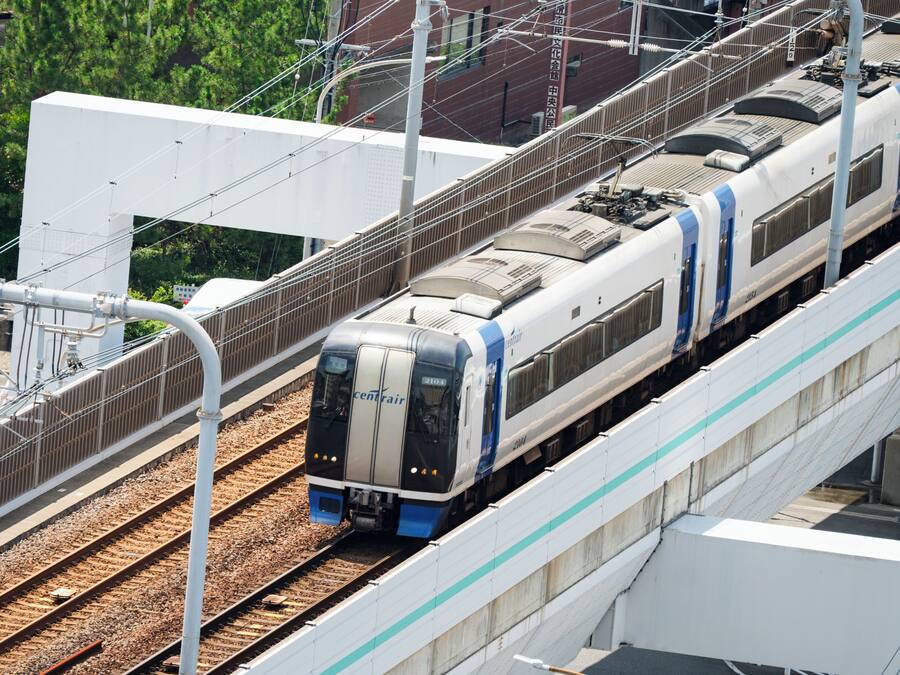 Ein Zug auf einer erhöhten Trasse mit modernem Design, umgeben von Infrastruktur und Grünflächen.
