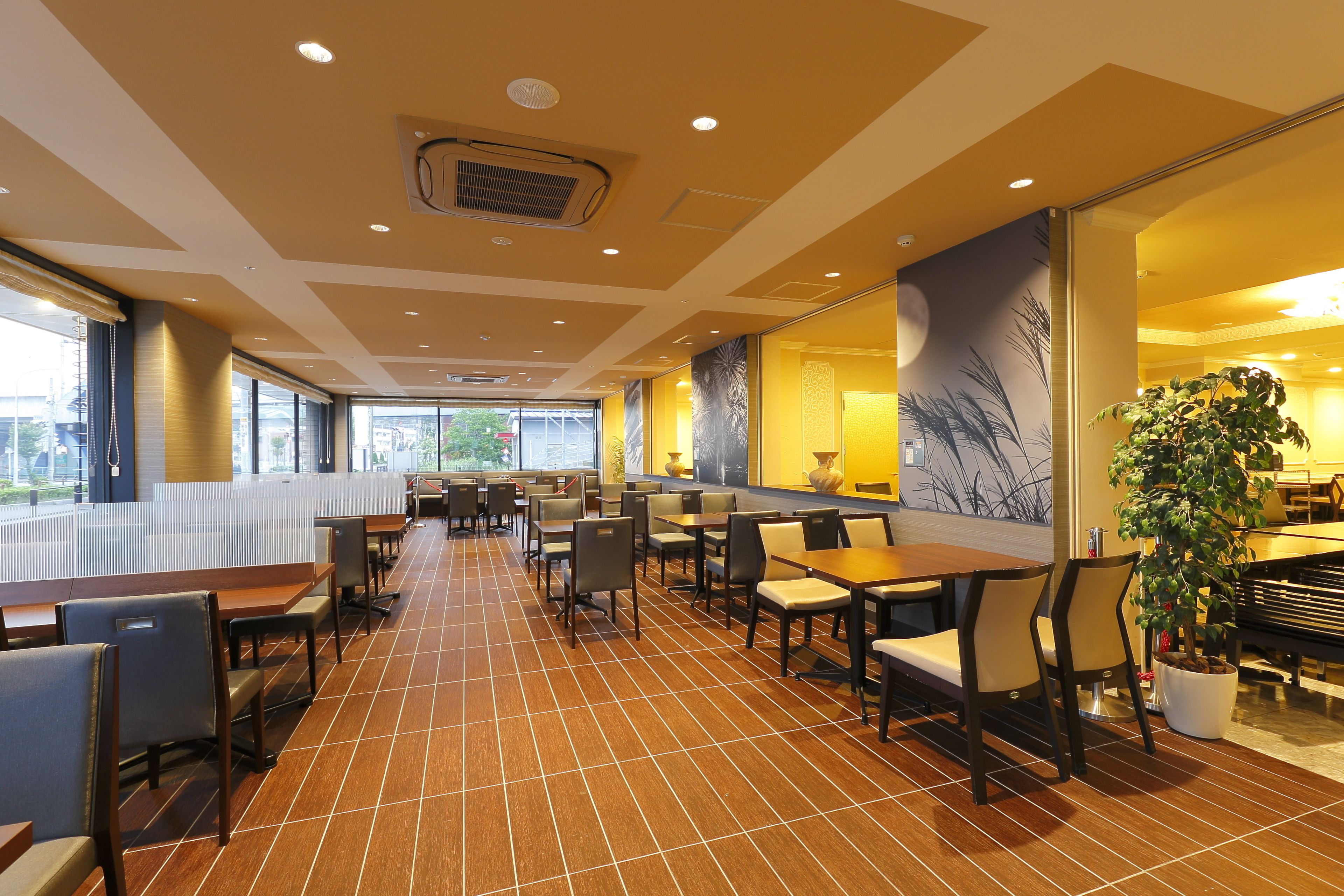 A spacious indoor area with multiple seating arrangements, including tables and chairs, and a large potted plant.