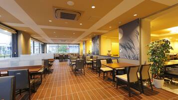 A spacious indoor area with multiple seating arrangements, including tables and chairs, and a large potted plant.