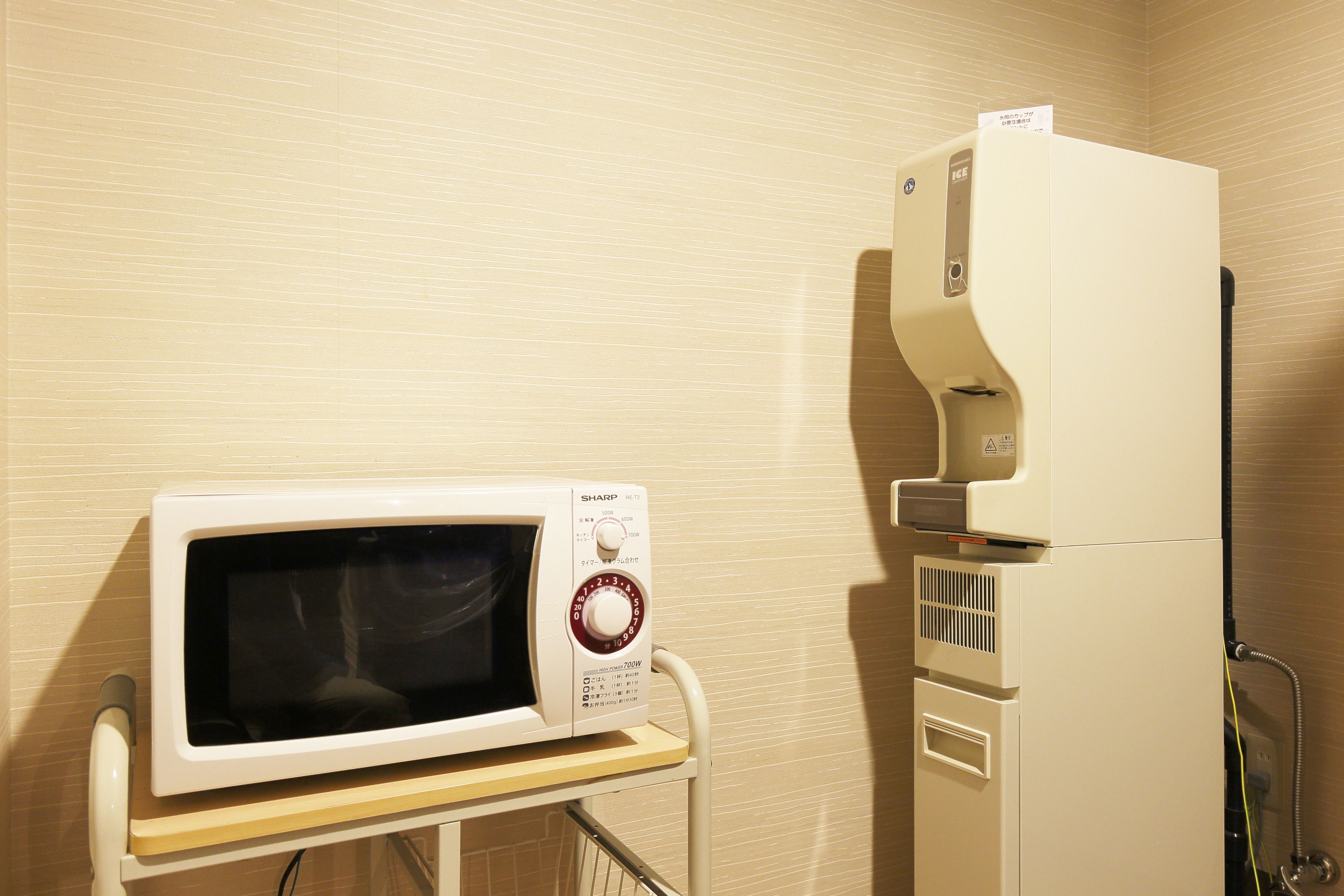 A microwave on a cart in a room with beige walls.