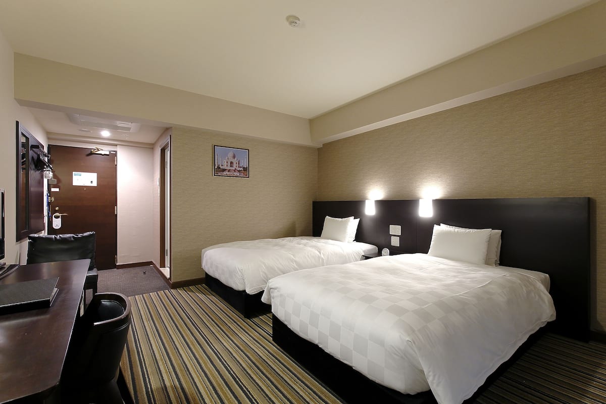 A hotel room with two beds, a desk, and a chair.