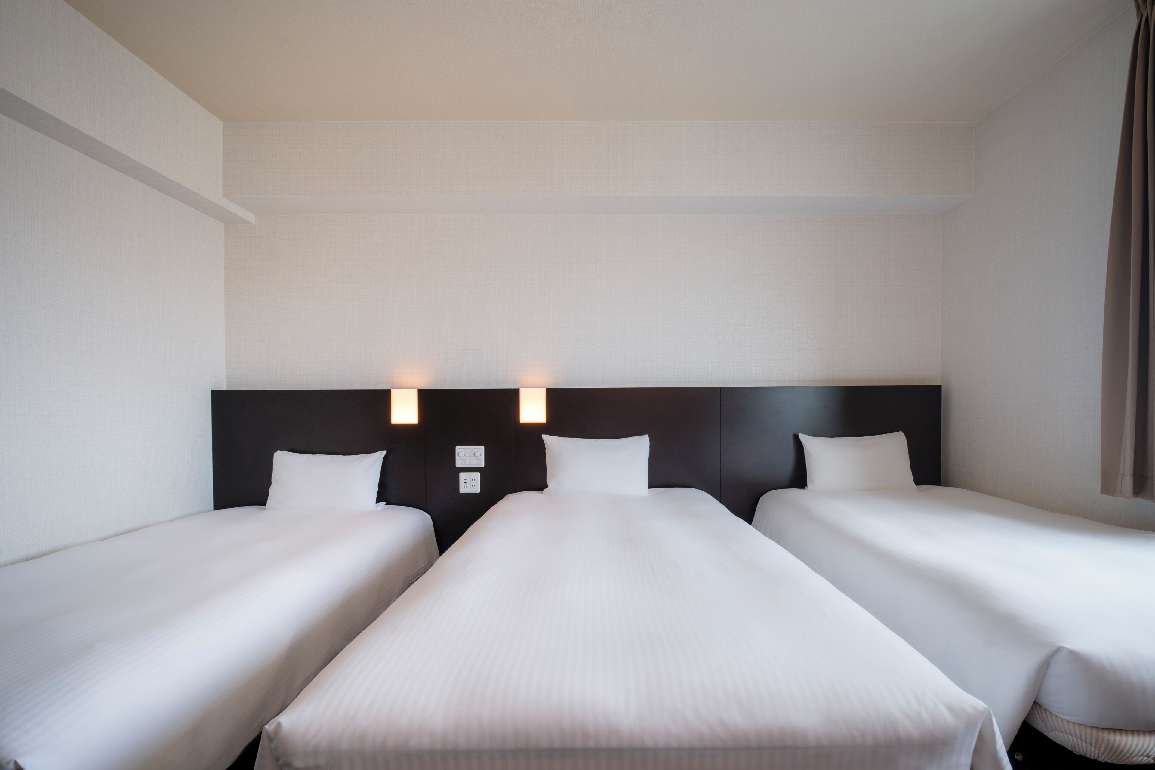 A hotel room with two single beds and a large bed, all with white linens.