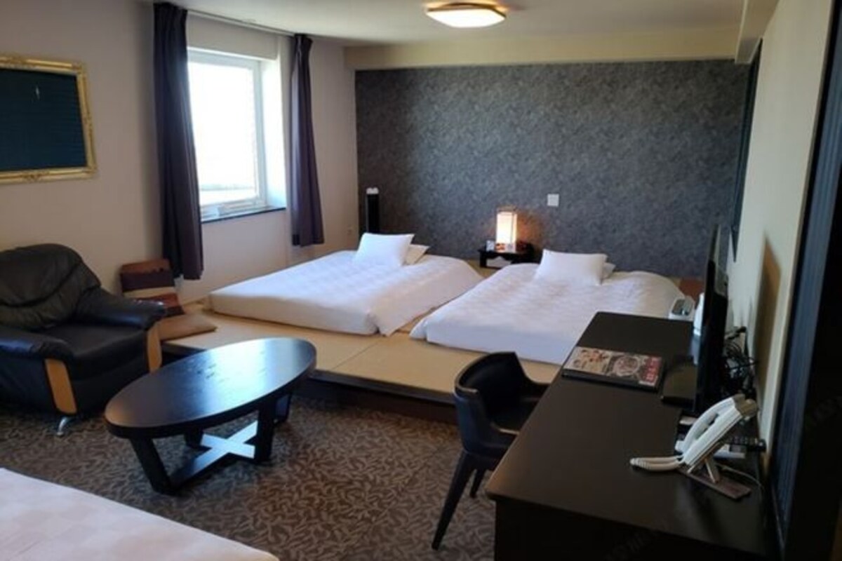 A hotel room with two beds, a desk, a chair, a small table, a telephone, and a window with curtains.