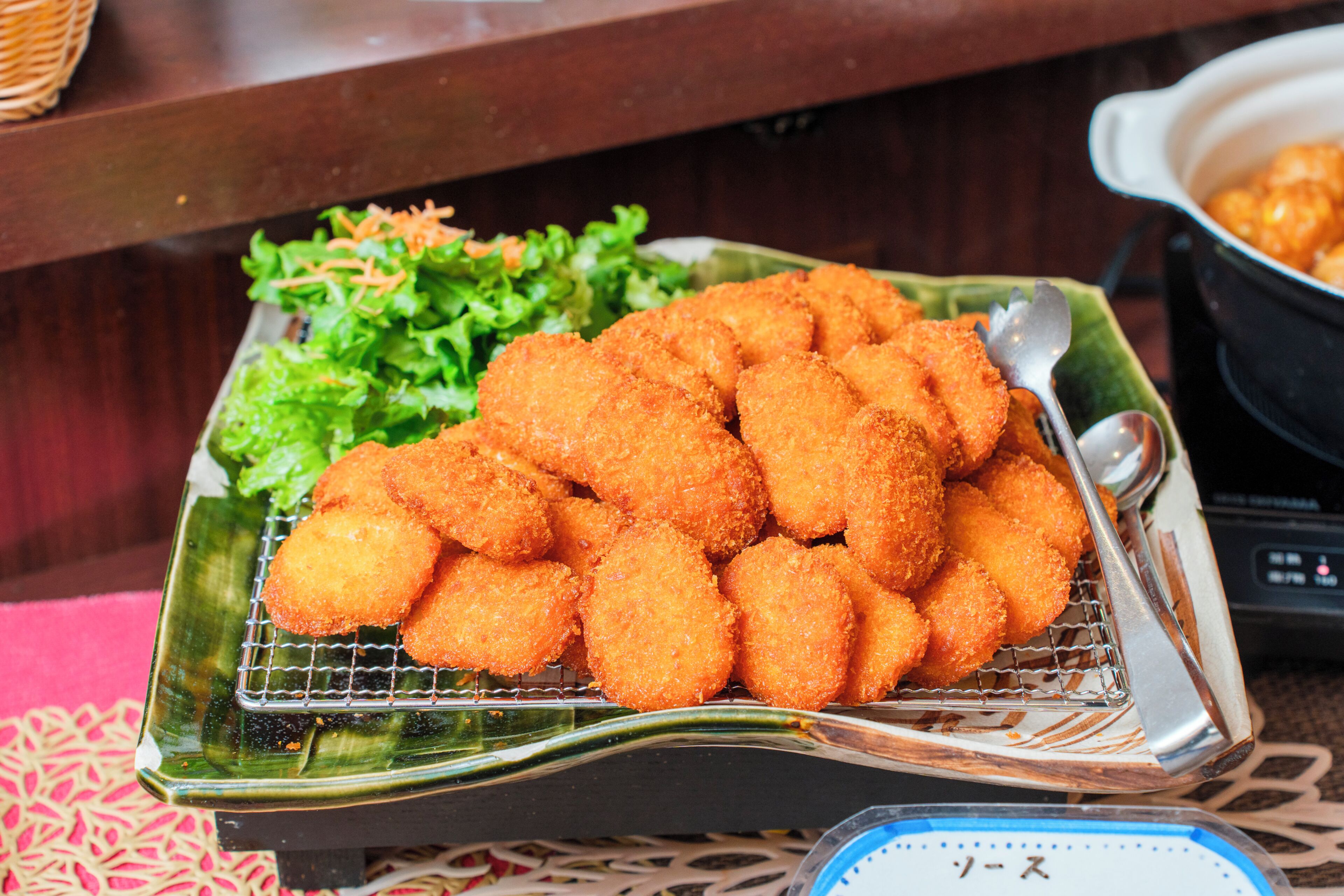 Une assiette de mets panés et frits, peut-être des croquettes, accompagnée d’une salade verte.