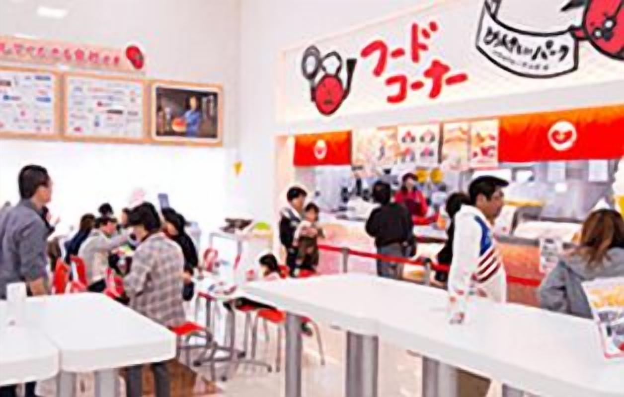 A busy food court with tables and chairs, and a counter with people standing in line.