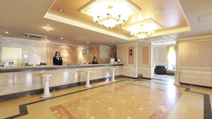A hotel reception area with a marble floor, a chandelier, and a reception desk with staff.