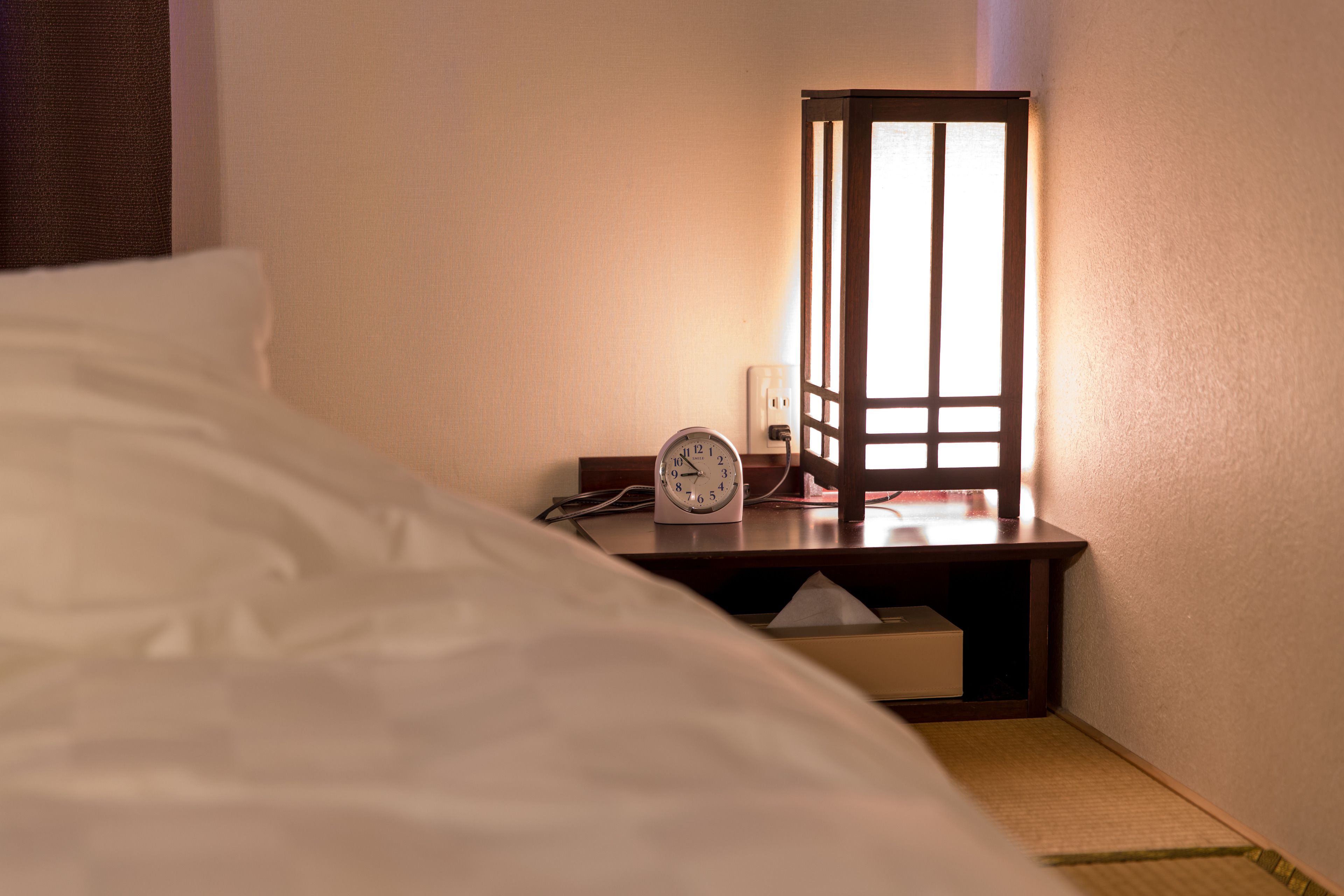 A neatly made bed with a bedside table that includes a clock and a lamp.