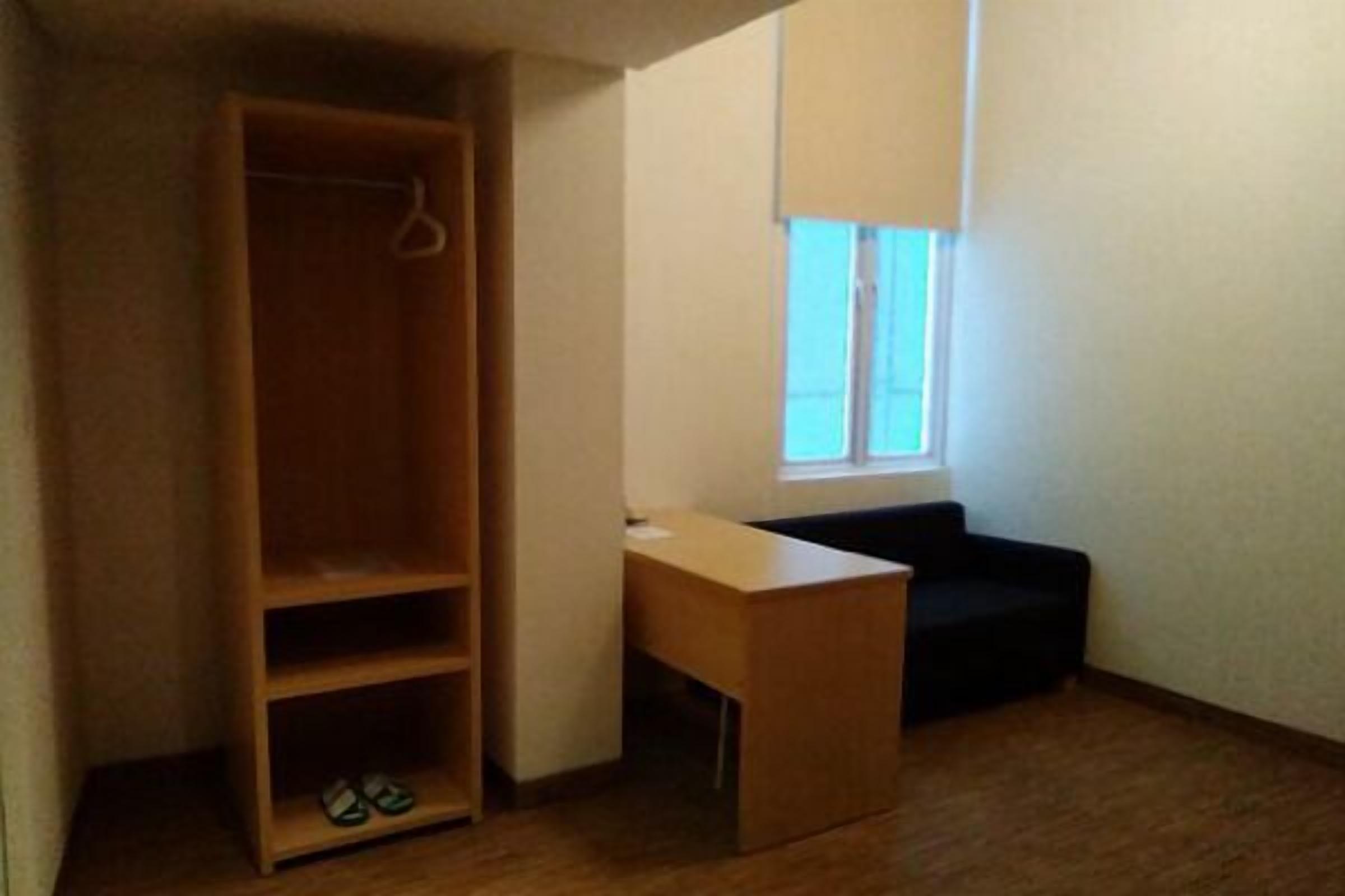A small room with a wooden wardrobe, a small desk, and a black sofa.