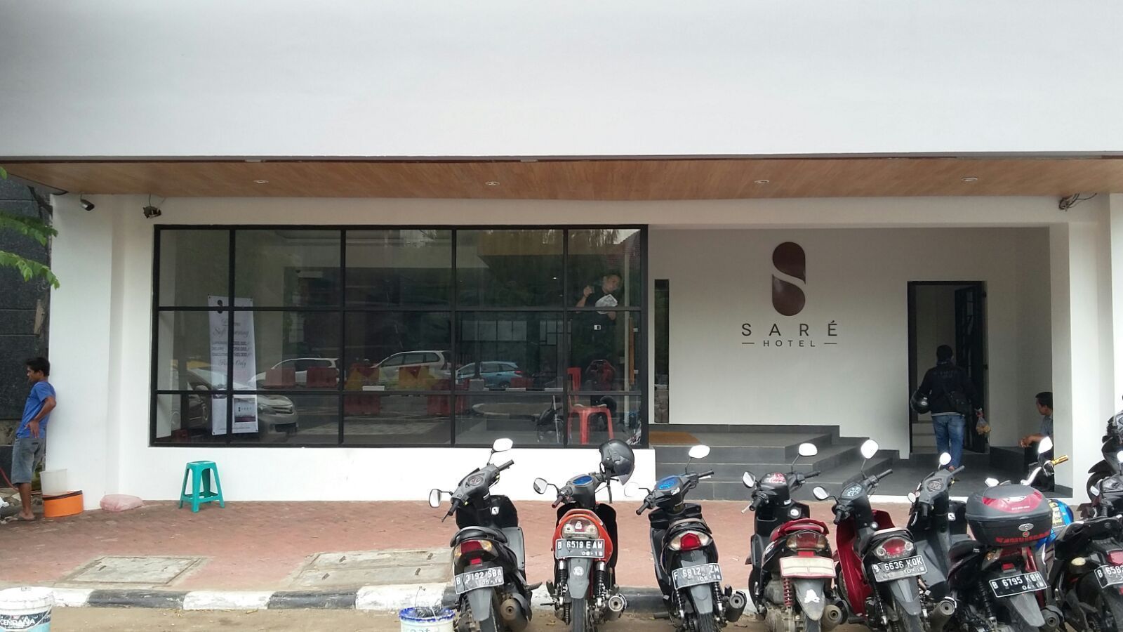 Entrada de un hotel con un amplio ventanal, un letrero que dice 'SARE HOTEL' y varias motocicletas estacionadas frente a él.