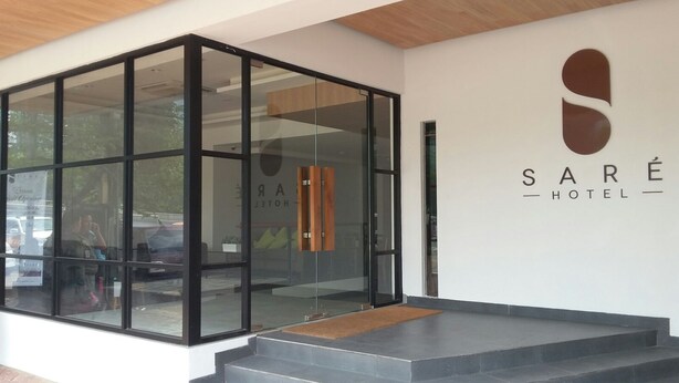 A modern hotel entrance with a glass facade, a wooden bench, and a sign reading "SARE HOTEL". - Sare Hotel (Jakarta)