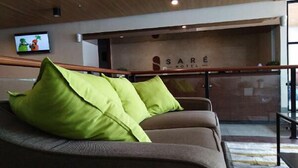 A hotel lobby with a sofa, green cushions, a television, and a sign for SARE HOTEL. - Sare Hotel (Jakarta)