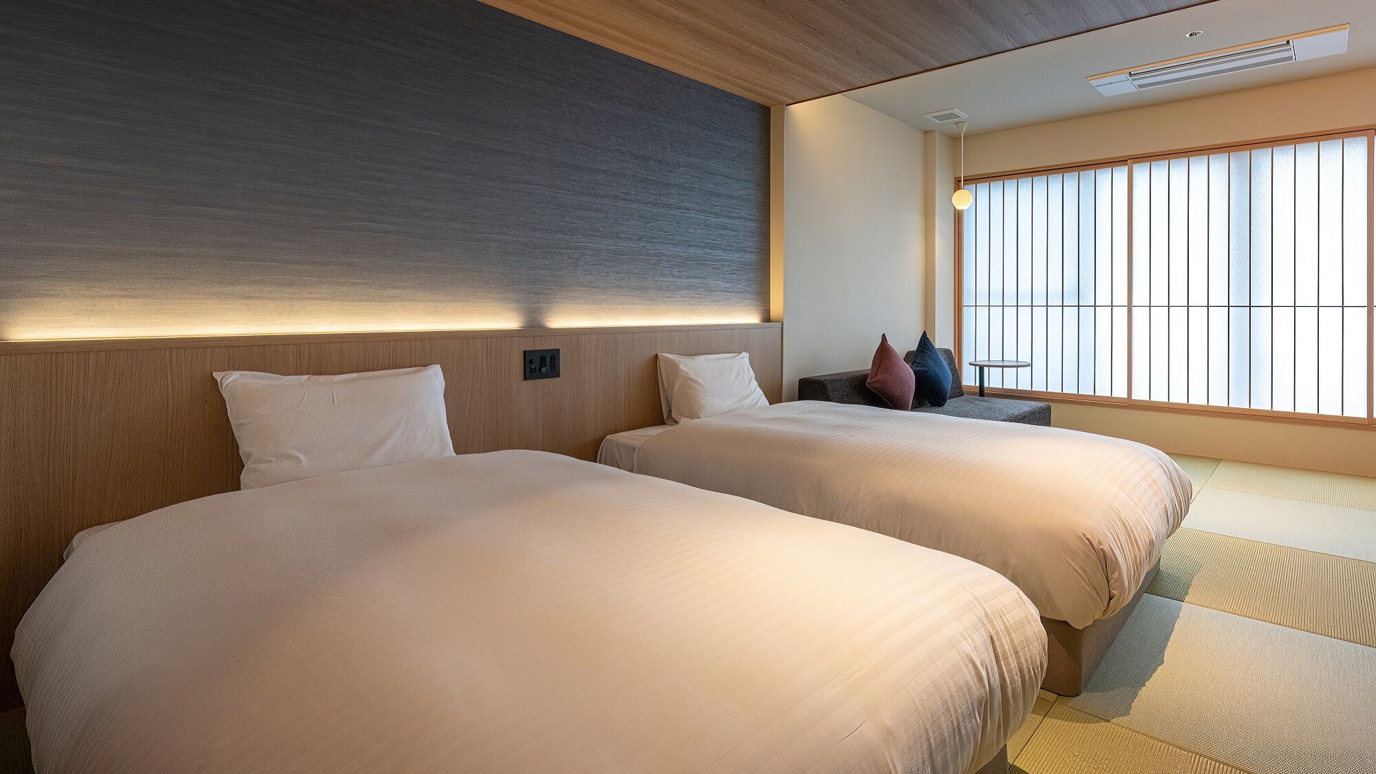 A hotel room with two beds, a sofa, a small table, and a large window with blinds.