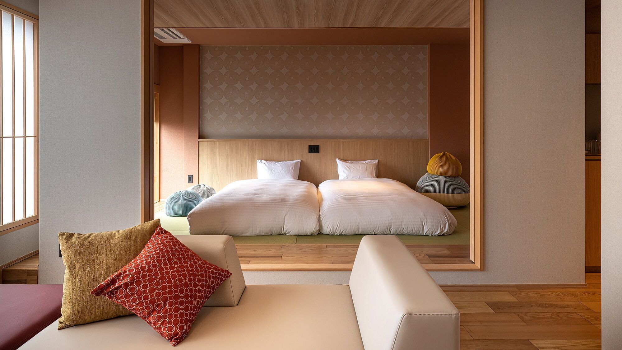 A modern hotel room with a large bed, two bedside tables, a sofa, and a window.