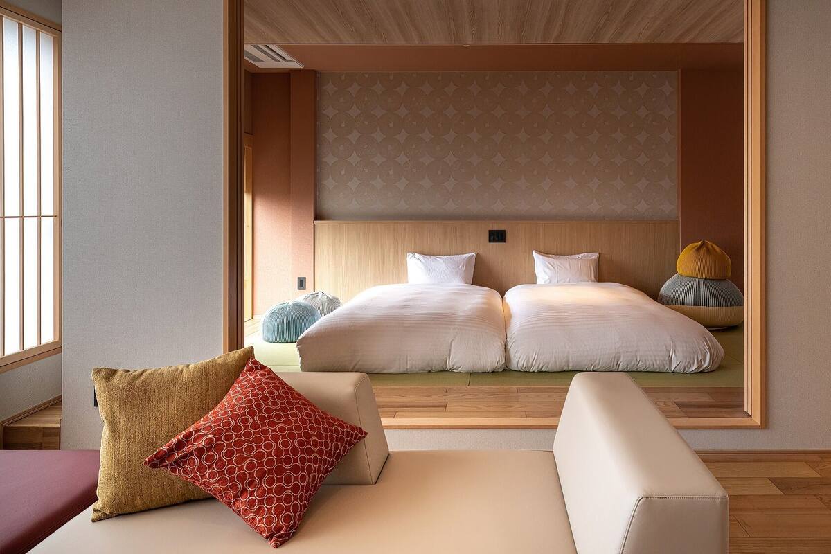 A modern hotel room with a large bed, two bedside tables, a sofa, and a window.