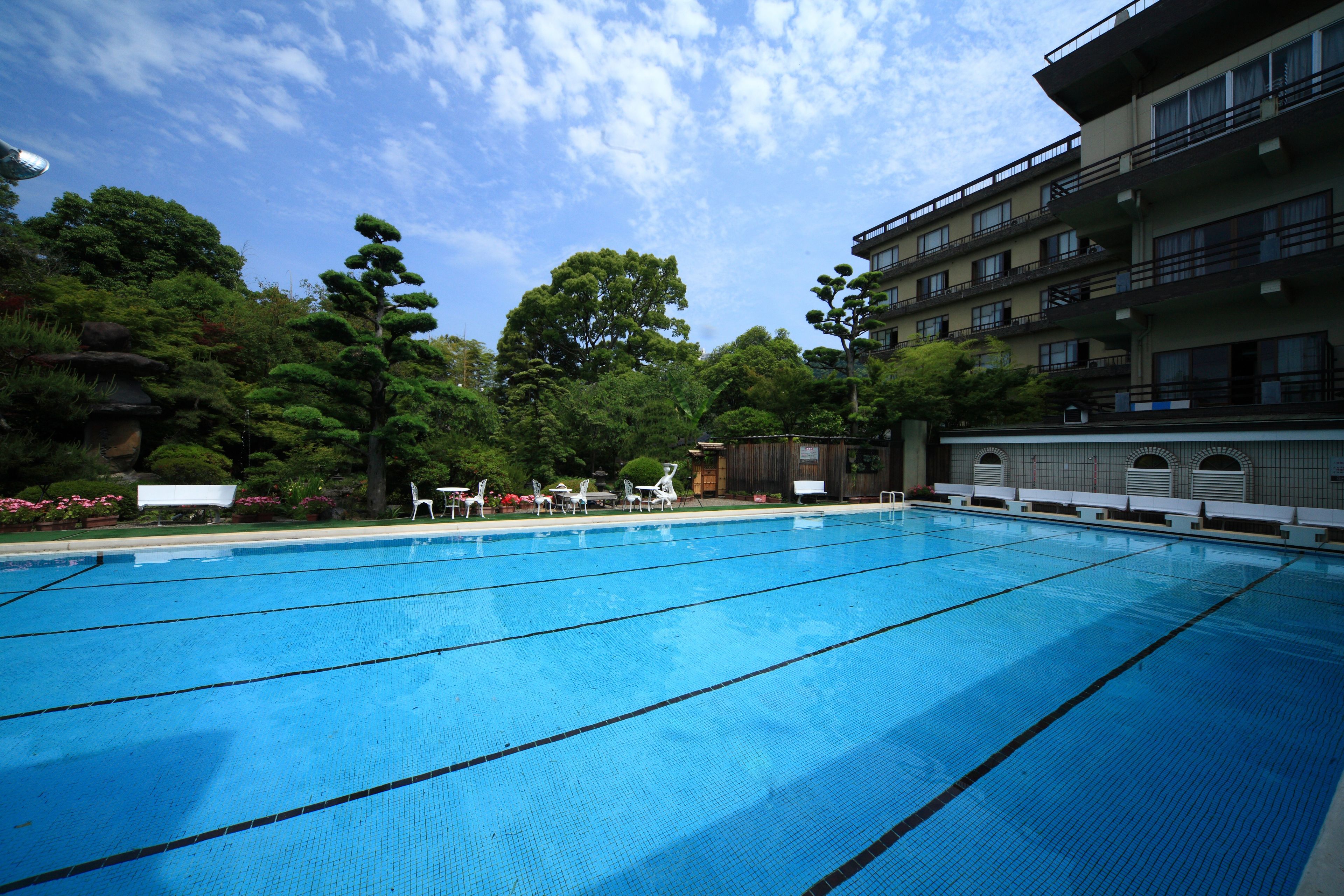 Una piscina con agua cristalina azul, rodeada de exuberante vegetación y un edificio de varios pisos con balcones.