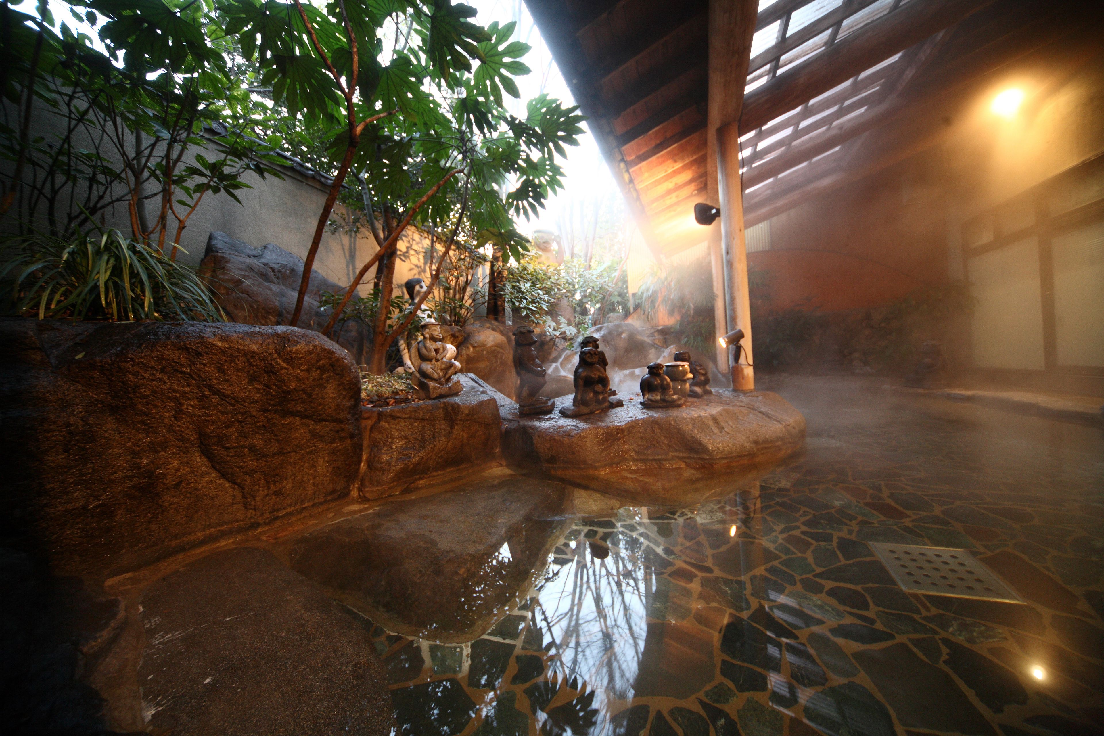 A hot spring area with stone statues, a tiled floor, and a wooden ceiling.