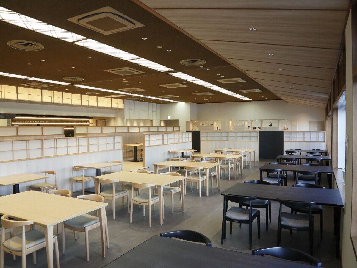 A spacious dining area with multiple tables and chairs, a long counter with a television, and a high ceiling with recessed lighting.