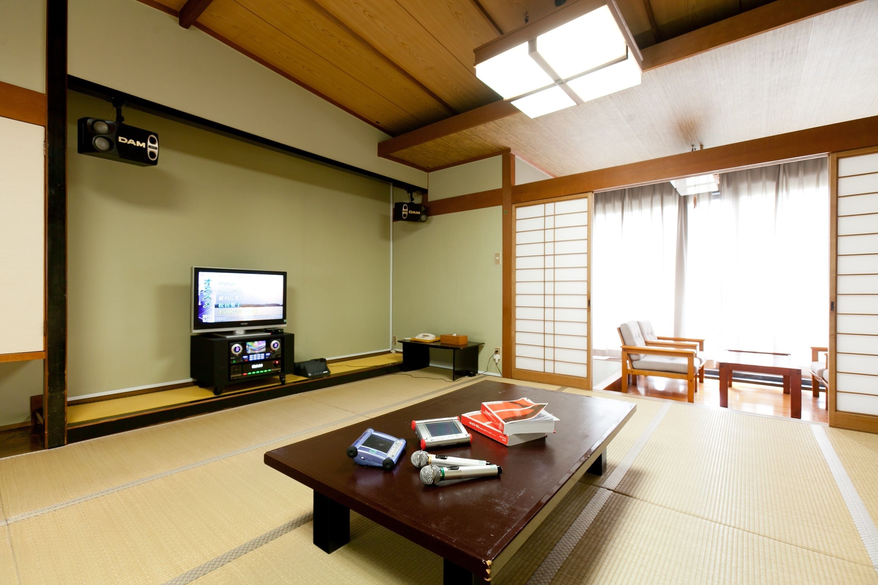 A traditional Japanese room with tatami flooring, a tatami mat table, a television, and a sliding door.
