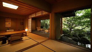 A traditional Japanese room with tatami flooring, a low table, and a view of a garden through a sliding door.