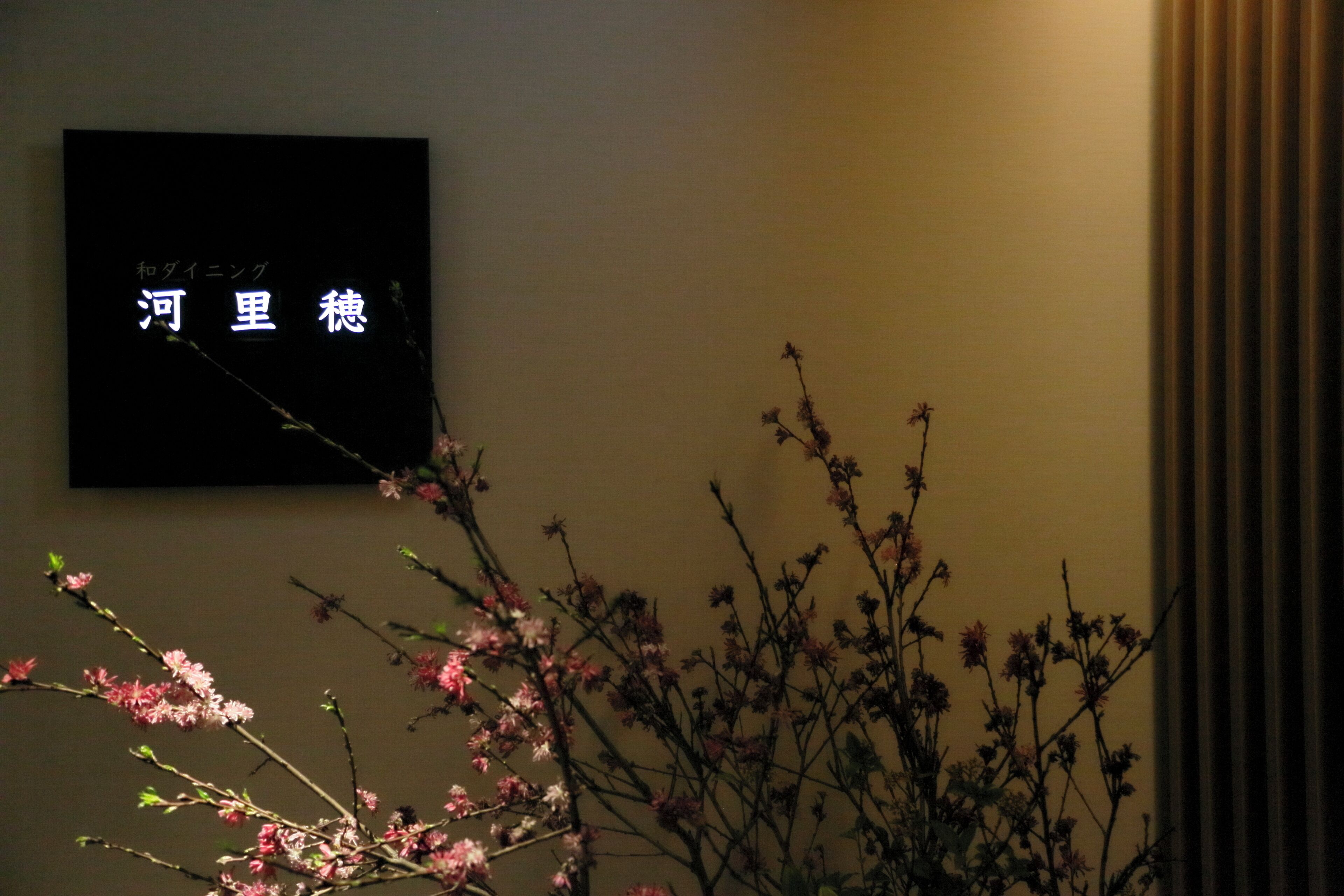 A wall with a sign in a foreign language, a branch with pink flowers, and a curtain.