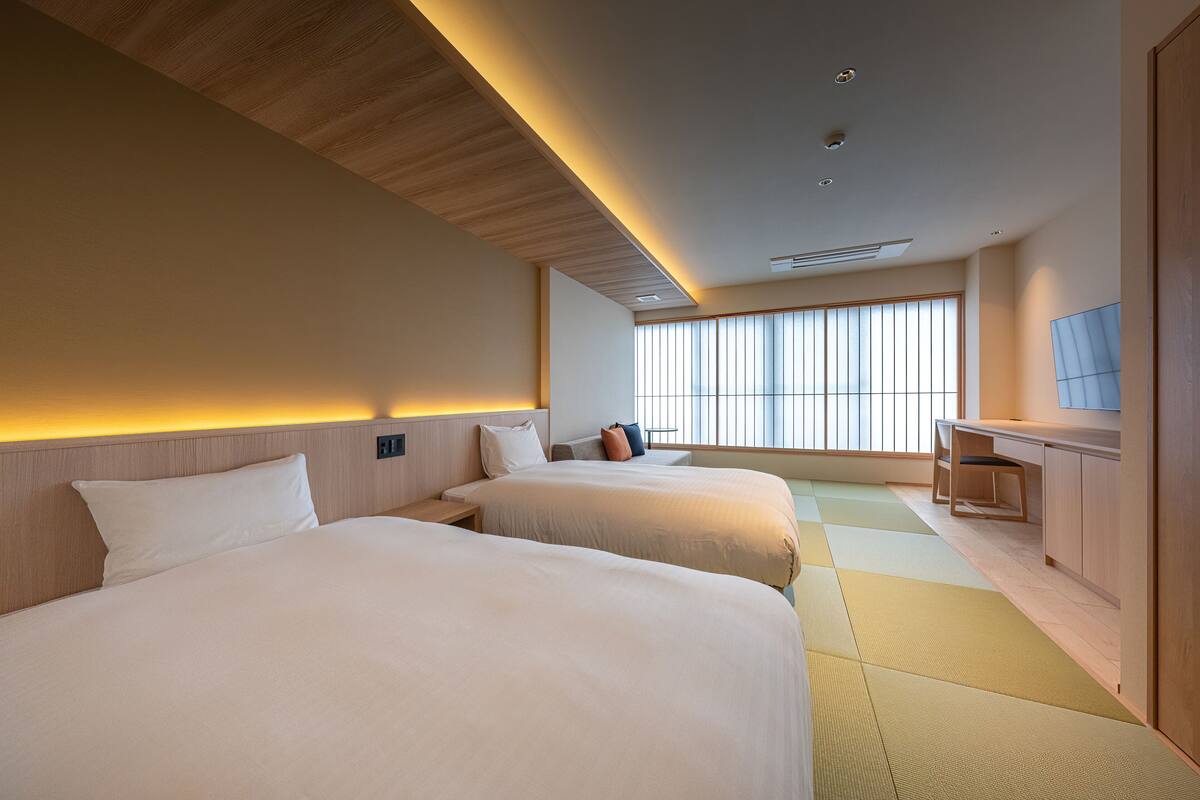 A hotel room with two beds, a desk, and a large window.